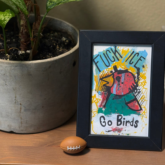 Framed artwork with a colorful design on a wooden surface next to a potted plant.