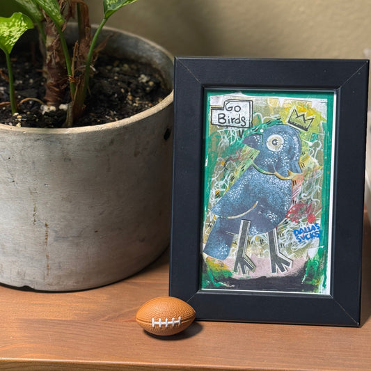 Framed artwork of a blue bird with a plant and football on a table