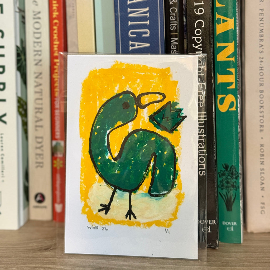 Card with a green bird design on a yellow background, placed among books on a shelf.